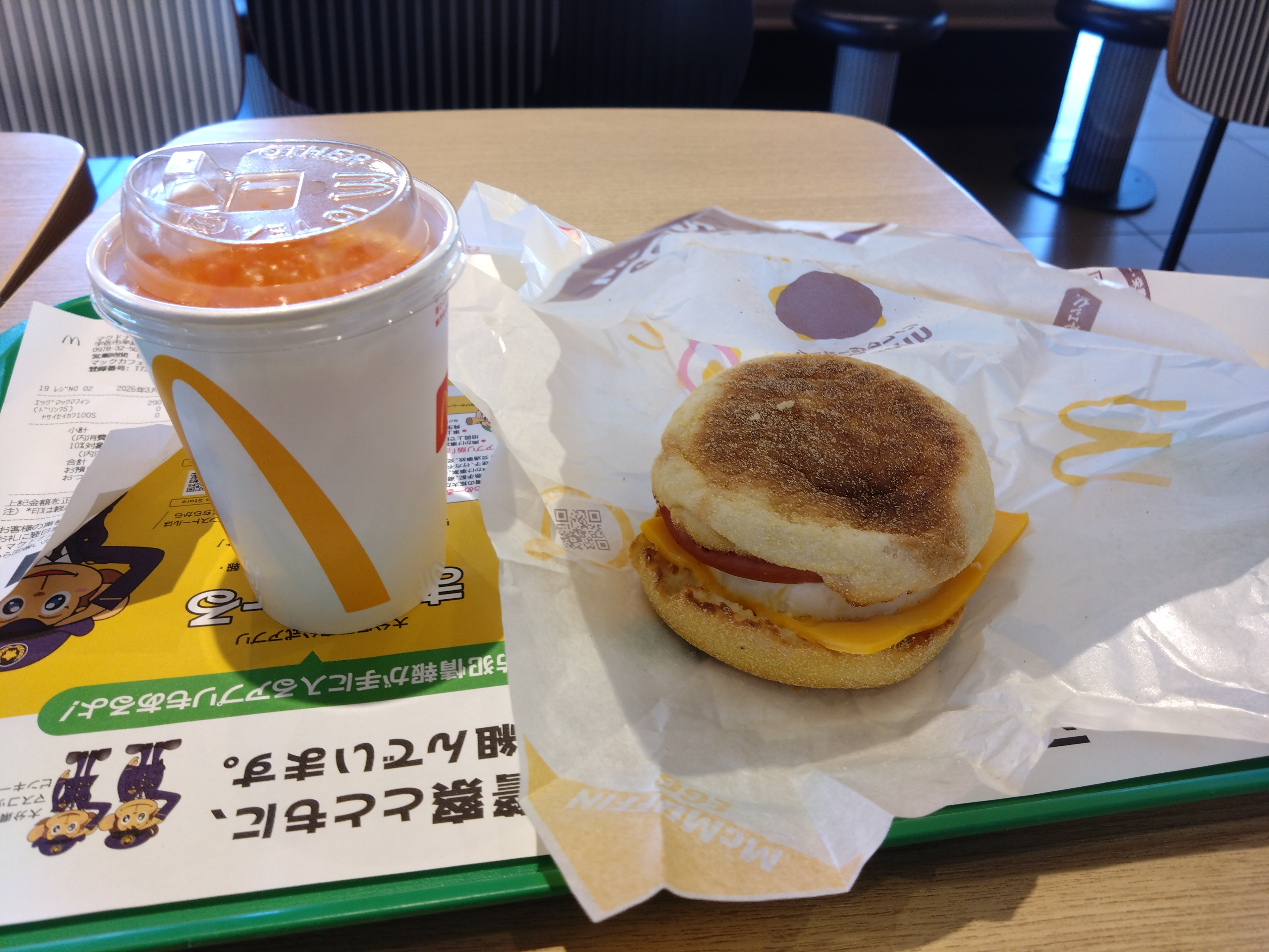 マクドナルドの朝食メニューが写っている。手前にはハンバーガーと飲み物がある。